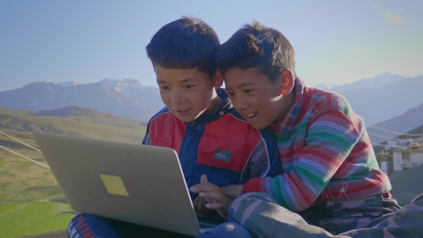 Young East Asian cheerful and smiling rural kids sitting together outdoors in the morning engrossed watching a funny video on a laptop with a beautiful landscape view of a mountainous region Royalty-Free Stock Footage #1081503281