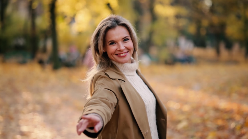 Attractive senior woman walking down the park, turns around with flying hair and looking at the camera. Happy relaxed lady walking on the autumn park enjoying.