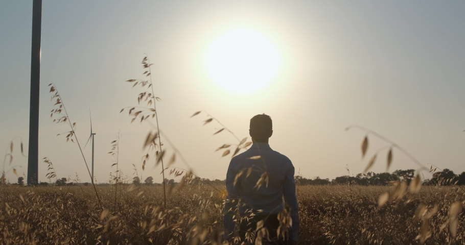 Young man fills with energy of bright sun putting hands up and standing in golden ripe wheat field in morning at countryside