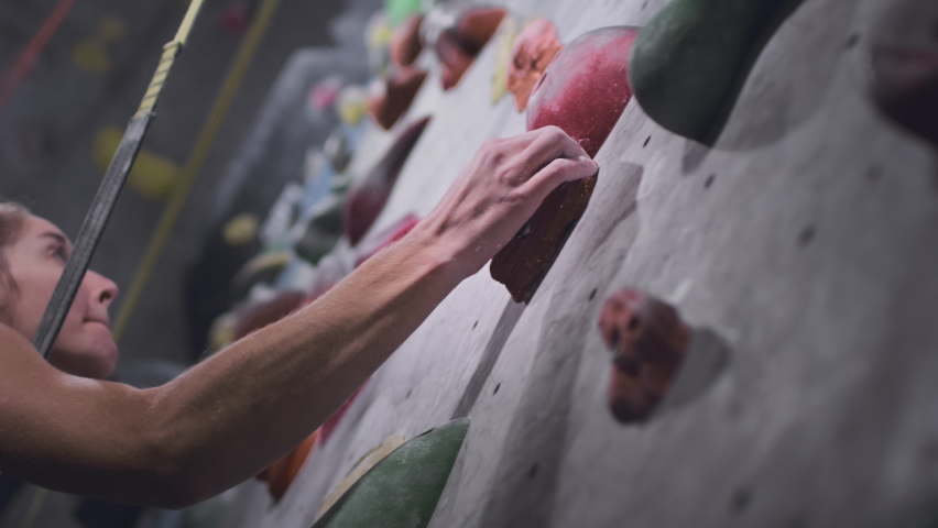 Sport athletic woman climbs up an artificial rock wall. Climbing solo in indoor gym. The girl grabs a stone with her hand. Hobby in the city, healthy lifestyle. Slow motion Royalty-Free Stock Footage #1081508036