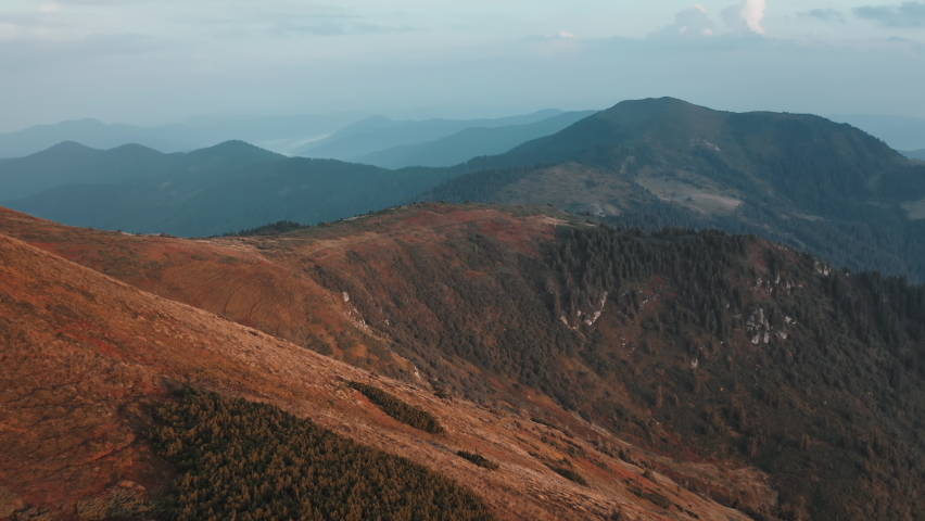 Aerial shot of Carpathian mountains. Mountain peaks, cliff, rocks, ridges, autumn orange grass, blue sky. Nature background. Beautiful wild landscape. Summer vacation travel, trekking, outdoor tourism
