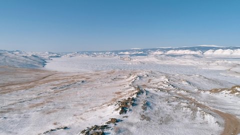 Aerial over the snow covered lands of Olkhon island in lake Baikal against the blue sky. Winter landscape of the lake Baikal.