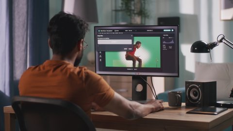 Back view of anonymous man integrating 3D graphic into video with real person while sitting at table and using computer in home office