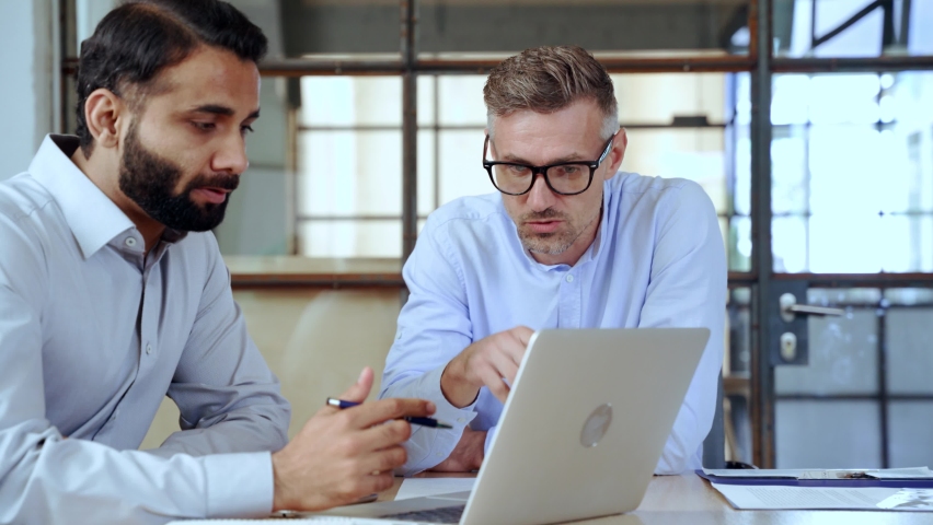 Two diverse business men discussing financial market data using laptop and digital tablet. Financial advisor broker manager consulting investor client about digital investment at office meeting. | Shutterstock HD Video #1081513610