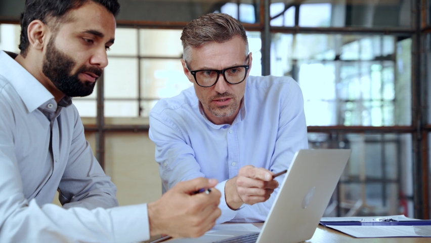 Two diverse business men discussing financial market data using laptop and digital tablet. Financial advisor broker manager consulting investor client about digital investment at office meeting. Royalty-Free Stock Footage #1081513610