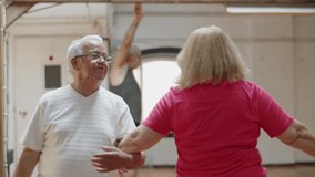 Medium shot of pretty senior couple dancing together in ballroom. Cheerful man and woman in eyeglasses swinging arm in arm, rehearsing, spending time together on weekend. Dance class concept - Powered by Shutterstock - Get 15% off with code: PIKWIZARD15