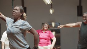 Cheerful dance teacher dancing with senior people in ballroom. Front view of enthusiastic woman warming up, showing arm movements to mature people attending classes. Dance class, hobby concept - Powered by Shutterstock - Get 15% off with code: PIKWIZARD15