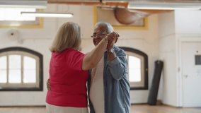 Medium shot of happy senior couple dancing together in ballroom. Cheerful Caucasian wife and husband dancing waltz, talking, spending time together during dance class. Sport, love, hobby concept - Powered by Shutterstock - Get 15% off with code: PIKWIZARD15