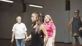 Cheerful female teacher showing dance movements to senior people. Tracking shot of excited young woman stepping side to side, learning dance combination in ballroom. Dance lesson, hobby concept - Powered by Shutterstock - Get 15% off with code: PIKWIZARD15