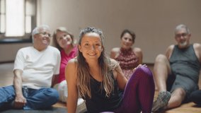 Long shot of female teacher sitting with dancing group on floor. Slow motion of senior people resting after dance class with instructor, looking at camera and smiling. Hobby, emotion concept - Powered by Shutterstock - Get 15% off with code: PIKWIZARD15