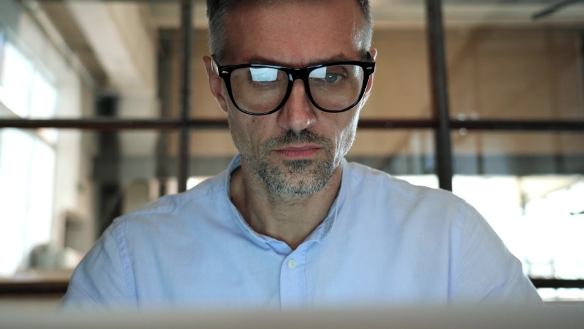 Mature concentrated business man trader wearing eyeglasses working looking at laptop computer screen reflecting in glasses thinking analyzing online trading market finance digital data. Close up view Royalty-Free Stock Footage #1081515689