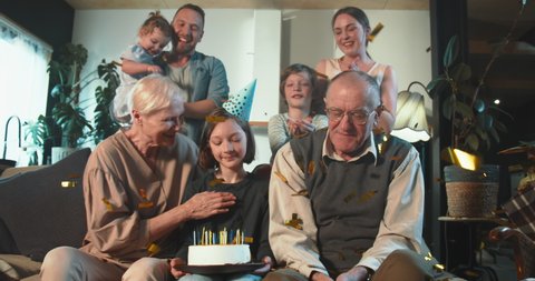 Multi generational family together. Happy smiling teen age girl celebrating birthday hugging grandparents on home couch.