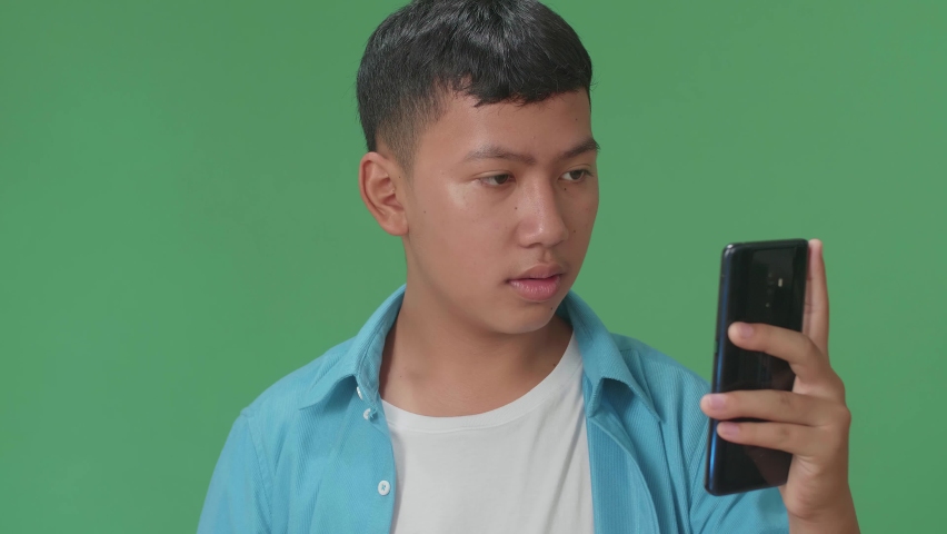 Young Asian Boy Celebrating With Mobile Phone While Standing On Green Screen In The Studio
