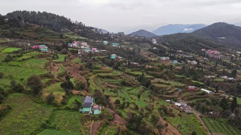 4k Aerial shot of terraced houses surrounded by green farm fields. Aerial view of Indian terrace farming in the month of October(Autumn). Drone view of the hills and a hilltop town on a cloudy day.