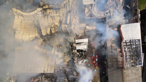 Aerial view of ruined building on fire with collapsed roof and rising dark smoke.