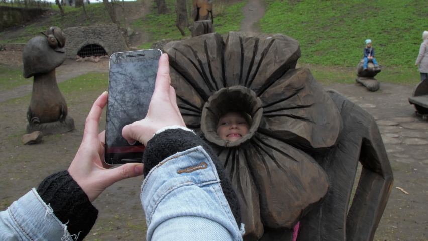 Mother holds smartphone and makes photo of daughter in park. Family recreation