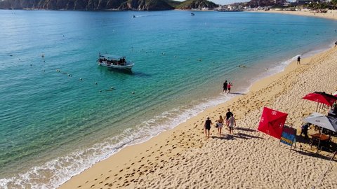 Cabo San Lucas , Mexico - 10 23 2021: Aerial view of people walking over a beach, towards a boat, in Cabo San Lucas, in Mexico - orbit, drone shot