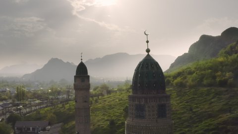 An aerial flight between the domes of the mosque against the background of the city, a misty green valley and large mountains in the rays of the contour sun. A beautiful landscape with stunning nature