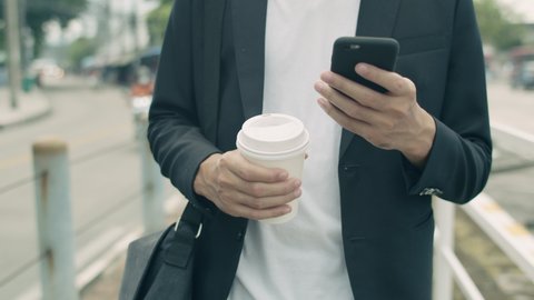 Close-Up of Asian businessman using his smartphone while walking on the street to the office in the morning.