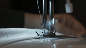 Needle for sewing machine in motion. The close-up of the sewing machine needle quickly moves up and down. The seamstress sews gray fabric in the sewing workshop. The process of sewing the fabric.	