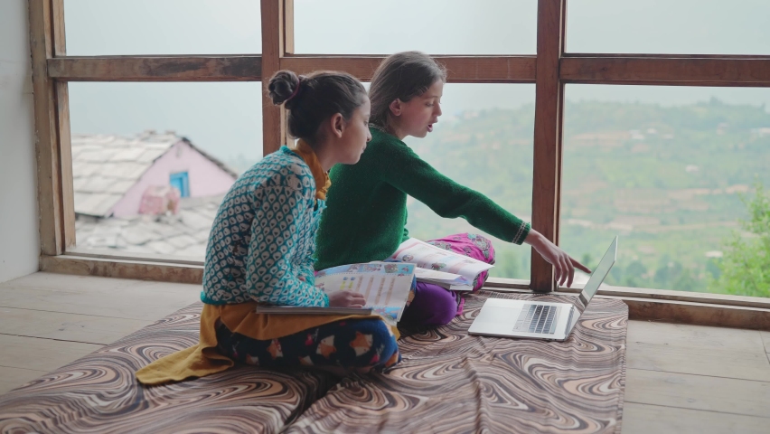 Two young village or rural school girls sitting indoors and using the laptop with the internet to study in an interior house set up with the green mountains in the back. learning and education concept Royalty-Free Stock Footage #1081552667