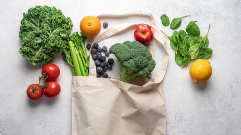 Stop motion animation of grocery shopping. Healthy vegetables and fruits putting in cotton bag on light background, top view