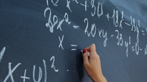 Female hand with chalk. Math faceless teacher writes examples for schoolchildren on blackboard. Student, pupil girl solves system of equations on chalkboard. Algebra, mathematics in classroom