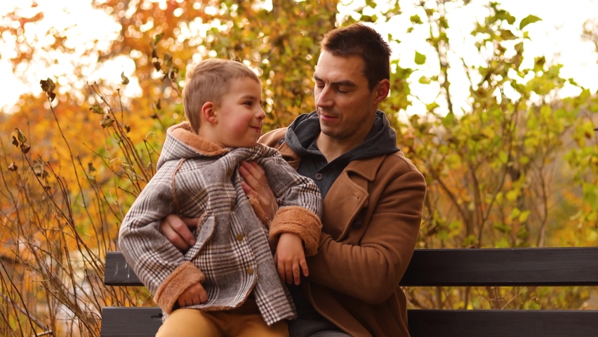 Handsome Caucasian father having fun with his adorable children. Autumn park with fallen fall leaves. Man and two kids, boys. Father talking with son. Family love.