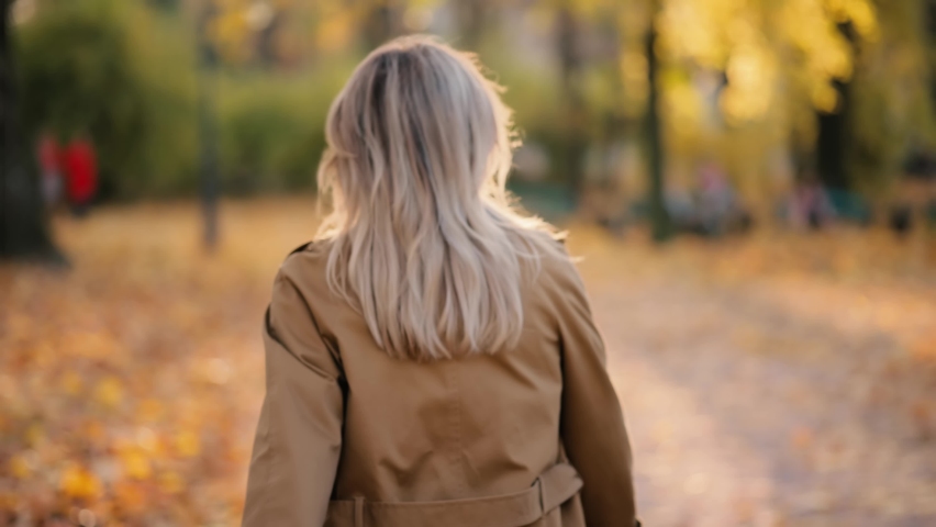 Attractive senior woman walking down the park, turns around with flying hair and looking at the camera. Happy relaxed lady walking on the autumn park enjoying.