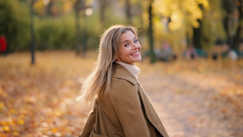 Attractive senior woman walking down the park, turns around with flying hair and looking at the camera. Happy relaxed lady walking on the autumn park enjoying.
