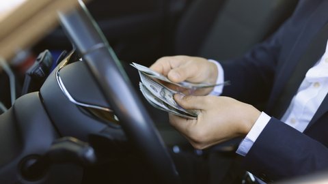 Man counting dollar bills sitting in a car. Close up of male hands count money cash. Concept of earnings or bribes, insurance or credit, investing. Man counting money cash at luxury car