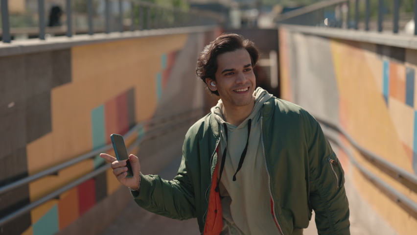 Happy young man listening music in wireless earphones while walking and dancing on street. Carefree male person using mobile app for enjoying favorite song outdoors. | Shutterstock HD Video #1081566242