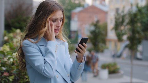 Business woman caucasian girl lady female looking in mobile phone feels shock upset worries about bad news problems of refusal financial notification mistake holds head with hand from stress in city