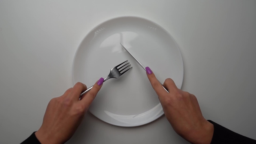 Female hands with a knife and a fork cut invisible food in an empty clean white plate, slow motion, close-up. top-down view. weight loss and overeating control concept. diet healthy lifestyle. | Shutterstock HD Video #1081572920