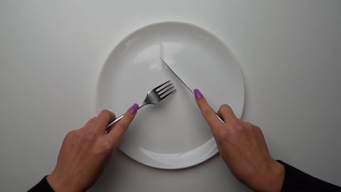 female hands with a knife and a fork cut invisible food in an empty clean white plate, slow motion, close-up. top-down view. weight loss and overeating control concept. diet healthy lifestyle.