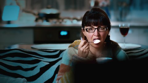 cinematic woman watching tv at home in the evening and eating ice cream, good mood