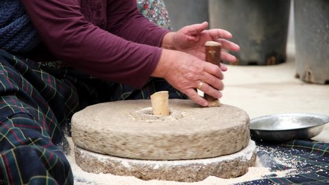The old woman is grinding flour in the stone mill with the old traditional method. Millstones for grinding wheat into flour, mill traditional production.