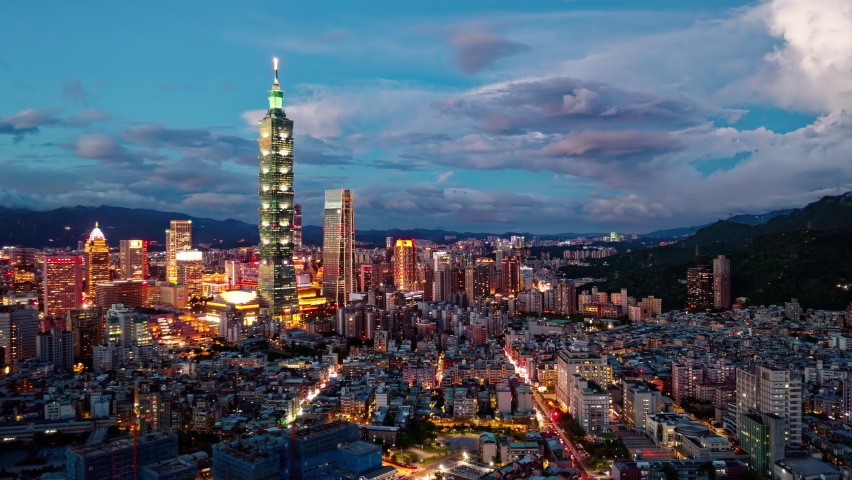Aerial hyperlapse of Downtown Taipei at dusk, vibrant capital city of Taiwan, with 101 Tower standing out amid skyscrapers in XinYi Commercial District and city lights dazzling under blue twilight sky Royalty-Free Stock Footage #1081582025