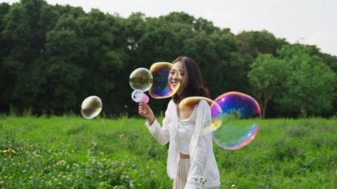 Slow motion of charming young asian woman blowing playing soap bubble in the spring field people relax lifestyle in the nature