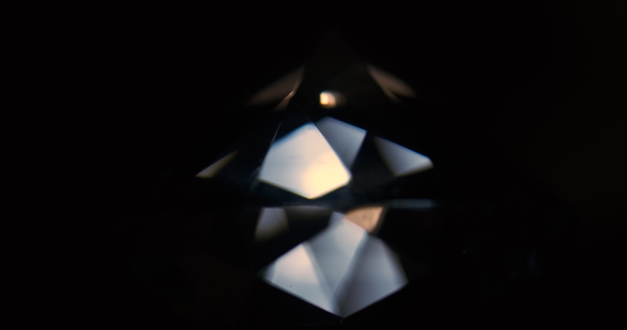 Rotation of the diamond. Reflection of light from the facets of the rhinestone. Close-up of a diamond on a black background. Isolated