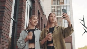 Low-angle tracking shot of young twin sisters with coffee in to-go cups laughing and recording video of themselves on mobile phone while walking down street together - Powered by Shutterstock - Get 15% off with code: PIKWIZARD15