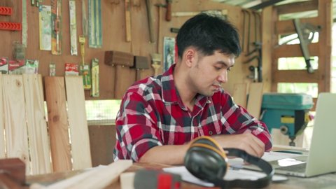 Asian man carpenter owns recheck wood and design. carpenter use mobile phone and discussing request from customer.Small business owner carpentry concept.