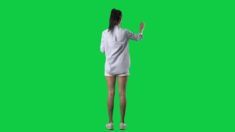Back view of stylish young business casual woman using touch screen interactive gestures. Full body isolated on green screen background