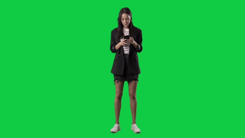 Happy relaxed young stylish woman in blazer using cell phone internet technology. Full body isolated on green screen background | Shutterstock HD Video #1081596761