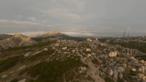 FPV video, mountain surfing, flying at high speed above the clouds with a granitic mountain range illuminated at sunrise. Mount Limbara (Monte Limbara) Tempio Pausania, Sardinia, Italy.