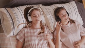 Handheld top view shot of young twin sisters lying on bed and listening to music in headphones - Powered by Shutterstock - Get 15% off with code: PIKWIZARD15