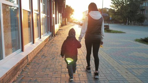 Happy family concept. Young mom walk with her toddler adorable son on the sunny sunset street.