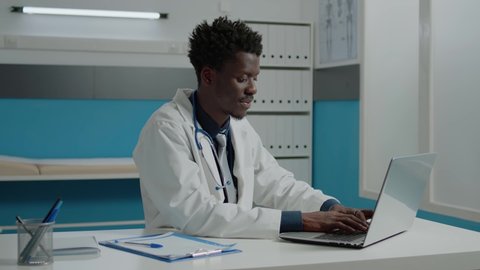 African american doctor using laptop while sitting at desk in hospital room. Black healthcare specialist working with technology for consultation in modern cabinet at medical facility
