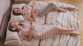 Handheld top view of young twin sisters lying on bed and listening to music with their eyes closed - Powered by Shutterstock - Get 15% off with code: PIKWIZARD15