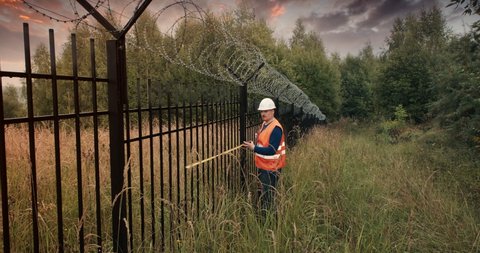 Worker with a measuring tape measure a fence with barbed wire. The concept of border closure, districts and specially protected objects. Access restriction and protection
